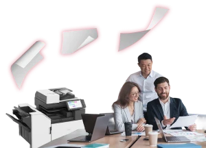 Three colleagues, one woman and two men, are gathered around a table with laptops and papers, looking at documents. In the foreground, a printer is visible on the left, with sheets of paper seemingly flying out of it towards the top of the image.